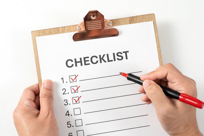 Hands checking items on a clipboard with a red marker.