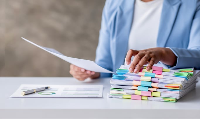 Professional reviewing documents beside a stack of organized paperwork.